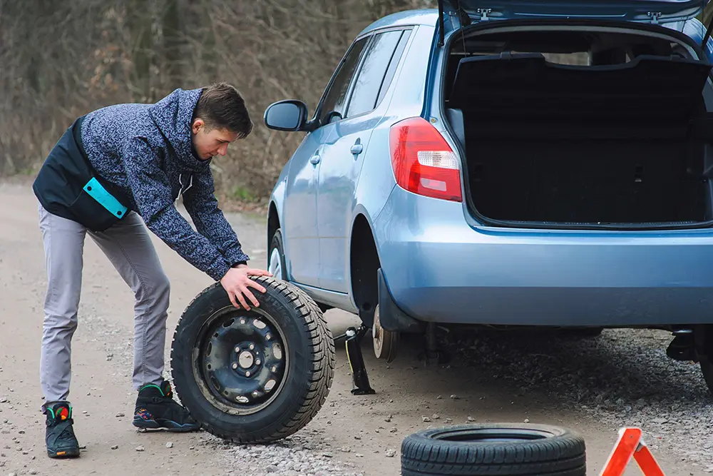 A driver changing a wheel at the roadside with the spare out of the boot